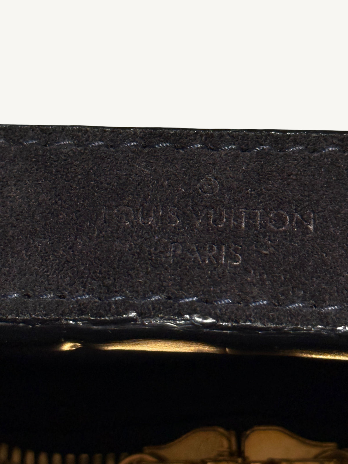 Close-up of a black Louis Vuitton leather interior label with embossed branding and a gold-toned zipper pull visible at the bottom.