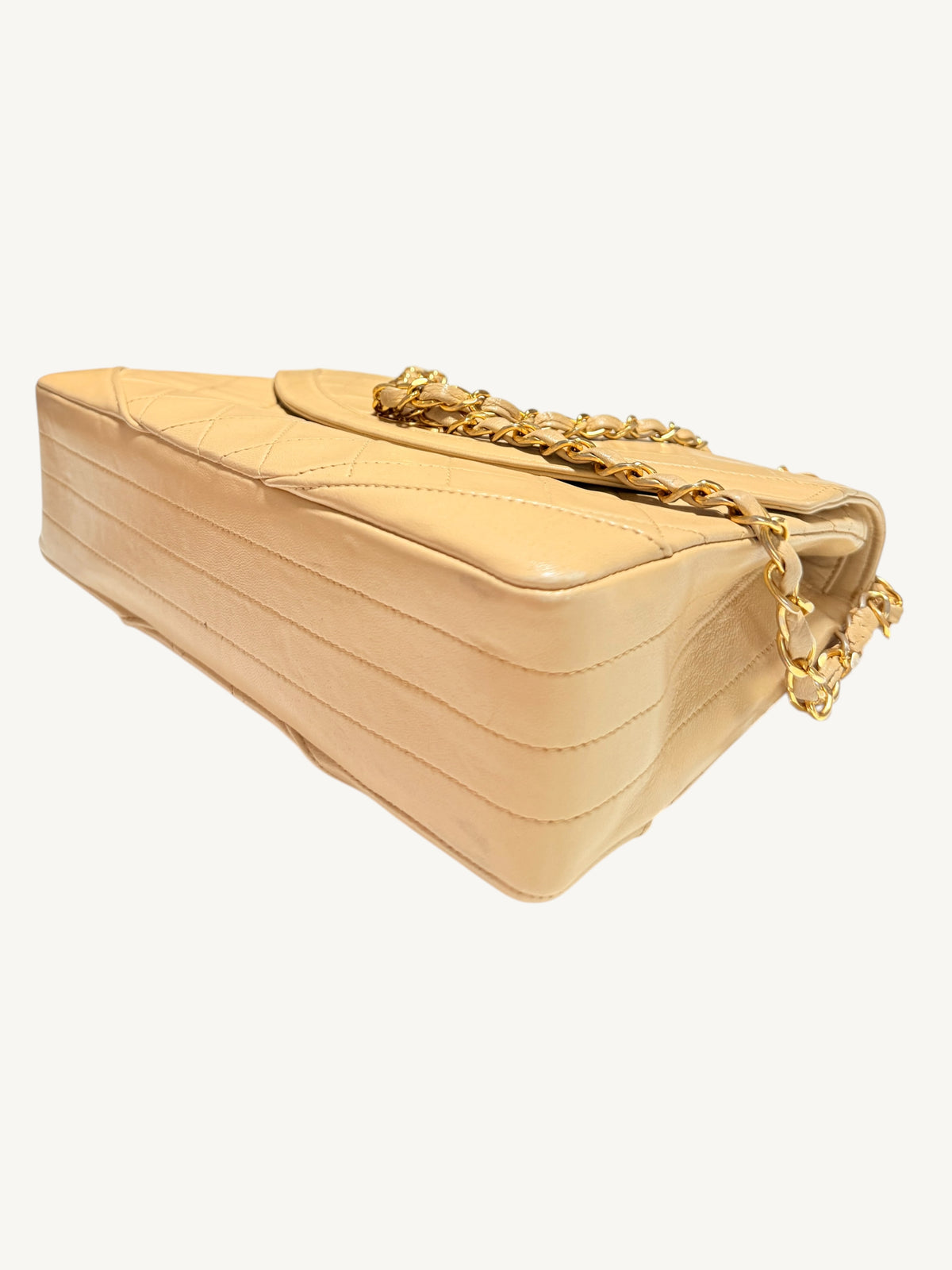 A beige quilted leather shoulder bag with a gold chain strap, shown from a three-quarters perspective against a plain off-white background.
