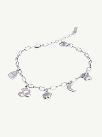 A silver chain bracelet with dangling charms including a small bird, a crescent moon, and two cherub figures, displayed on a light cream background.