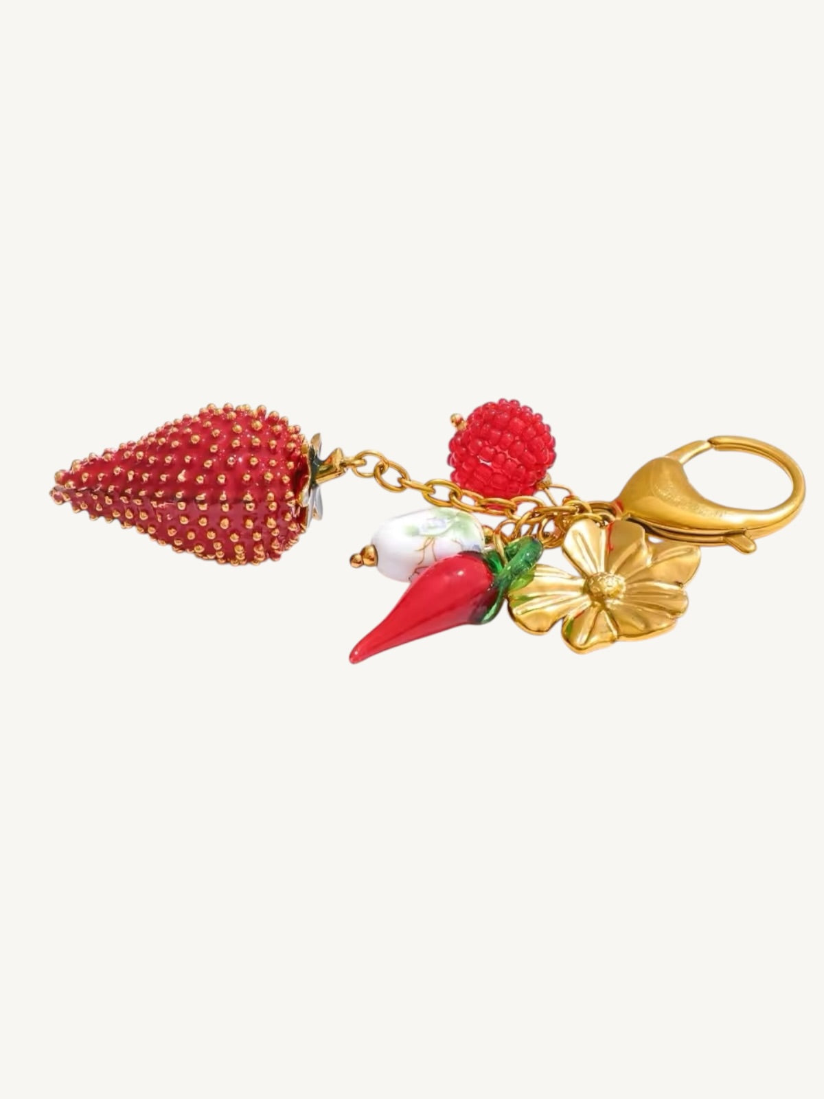 A strawberry-themed gold keychain featuring a large textured red strawberry, a small red raspberry, a white pearl, a red carrot charm with green leaves, and a gold flower, all attached to a gold clasp on a light gray background.