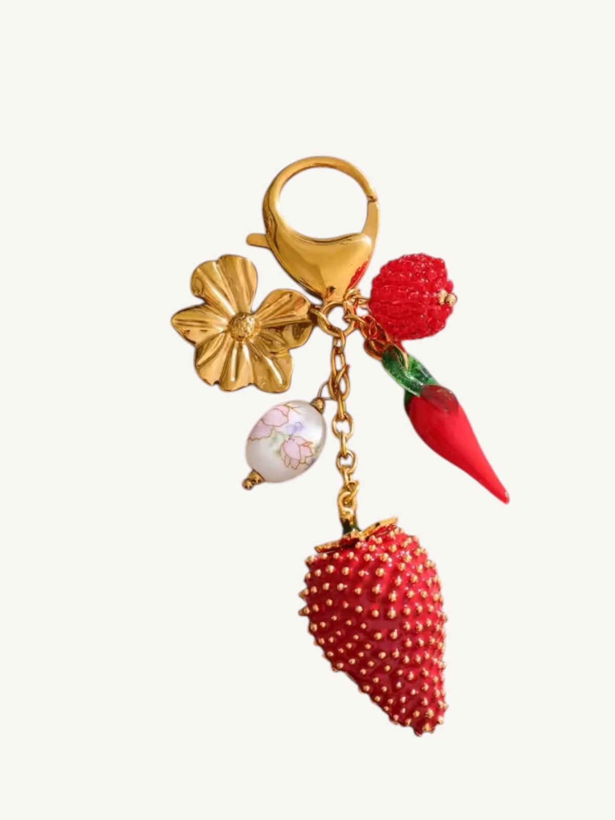 A gold-tone metal keychain charm featuring a flower, a small white floral bead, a red strawberry, and a red chili pepper, all attached to a gold split ring.