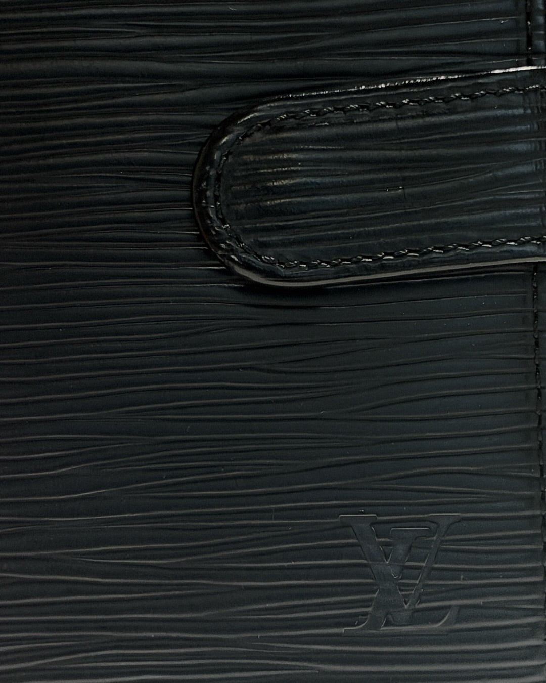 Close-up of embossed LV logo, black Epi leather texture and stitched leather snap tab