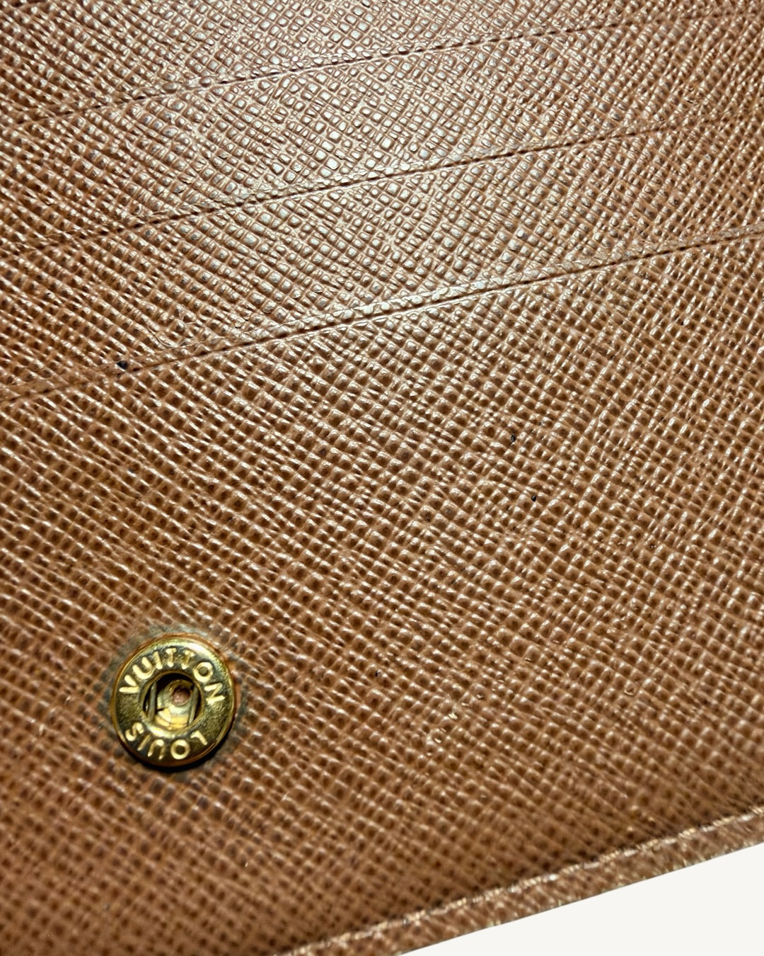 Close-up of Louis Vuitton engraved press-stud snap on textured brown interior beside card slots