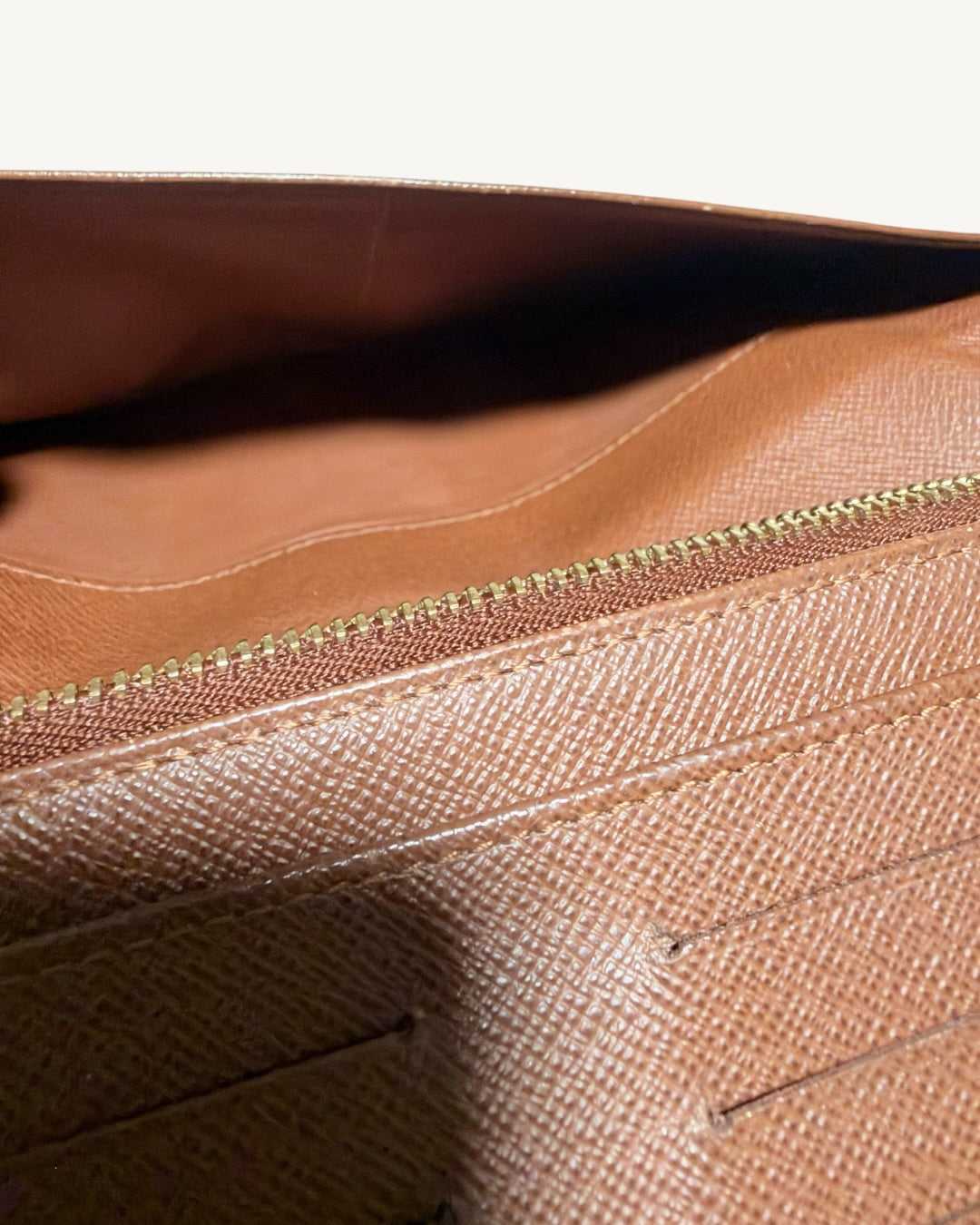Close-up inside brown wallet slip pocket with stitched divider and zipper teeth in foreground