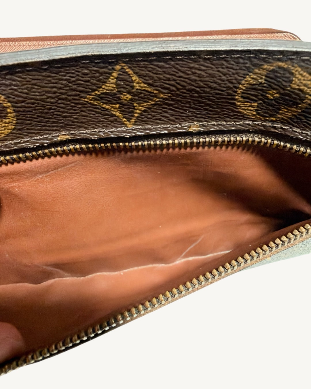 Exterior zip pocket opened to show brown lining beneath Monogram canvas and zipper teeth