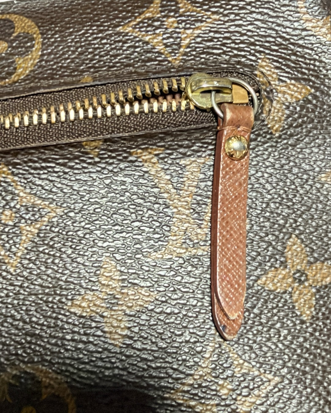 Detail of exterior zipper slider, brown leather pull and gold-tone rivet on Monogram canvas