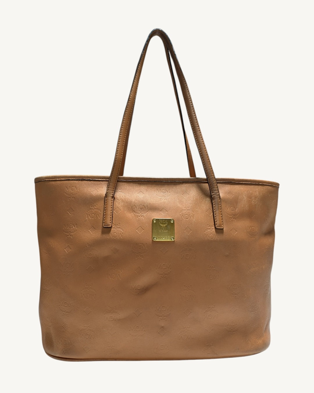 Front view of MCM cognac embossed leather tote with dual shoulder straps and gold-tone logo plaque.
