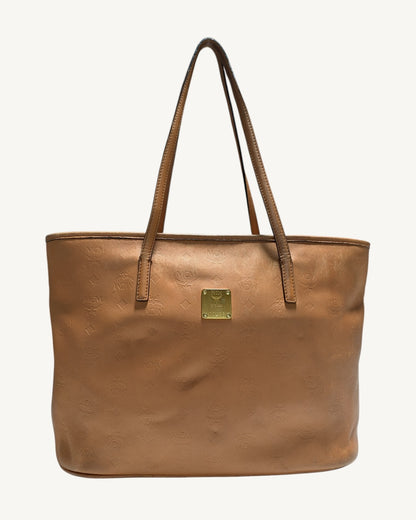 Front view of MCM cognac embossed leather tote with dual shoulder straps and gold-tone logo plaque.