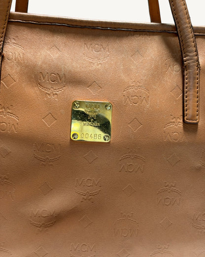 MCM tote front panel close-up showing embossed monogram, leather creasing and gold-tone plaque.
