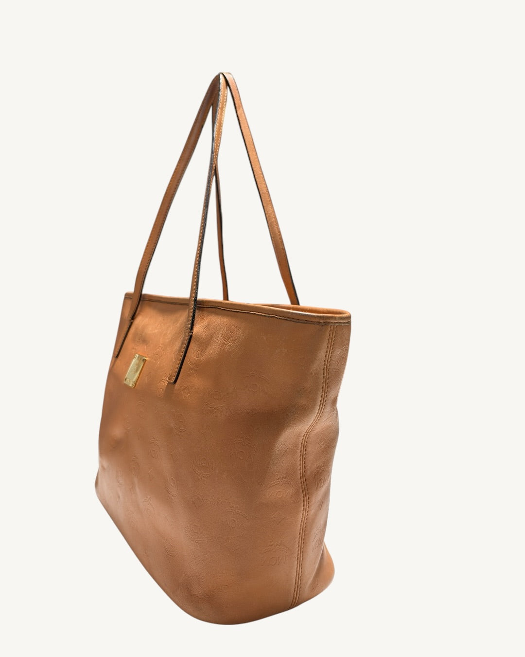 MCM cognac tote angled view showing the right side seam, front plaque and long leather straps.