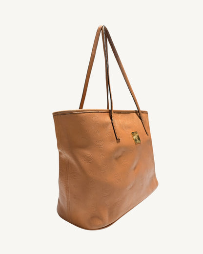MCM embossed leather tote angled view showing the left side seam and creased front panel.
