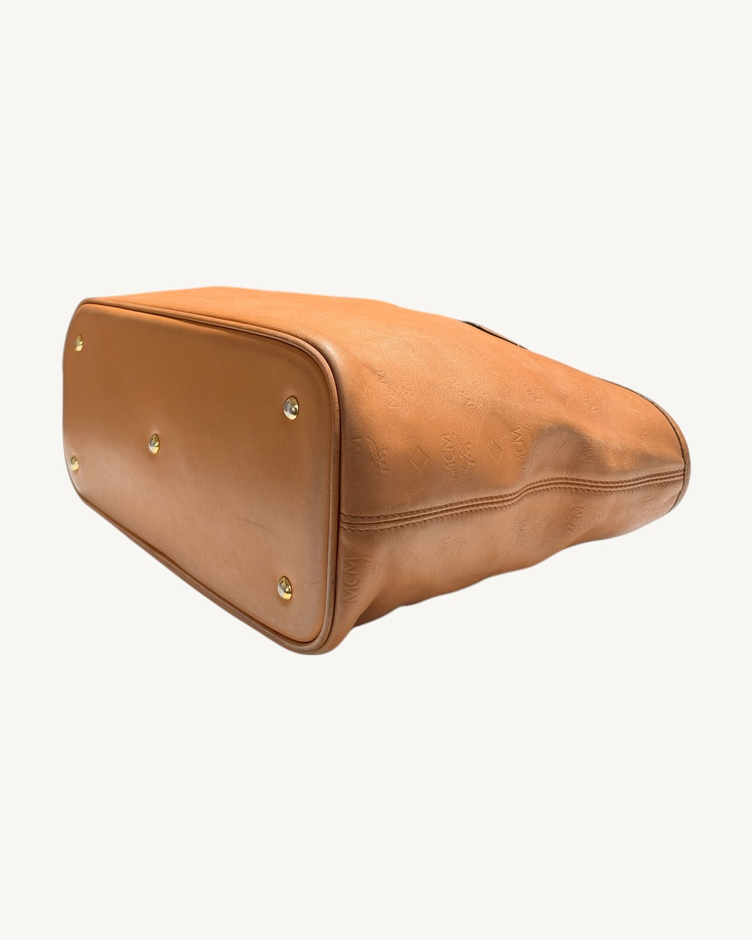 MCM tote underside angled from one end, showing base feet, corner piping and stitched side seam.