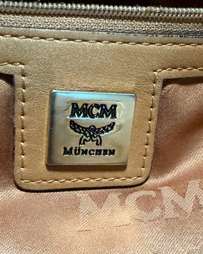 Interior MCM München logo plate on a stitched leather patch beside monogram fabric lining and pocket zipper.