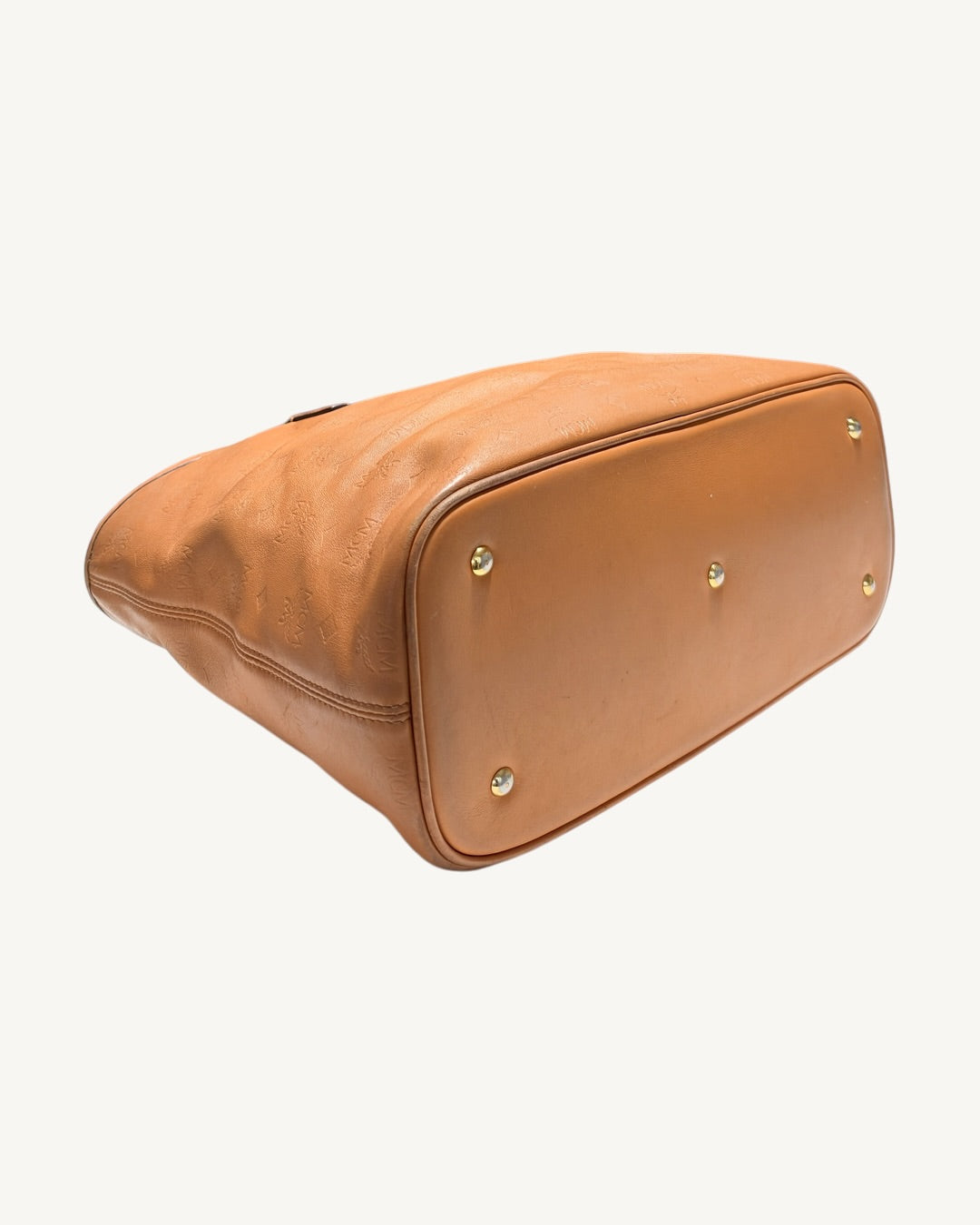 Low angled view of MCM tote base, showing metal feet, smooth cognac leather and adjoining embossed panel.