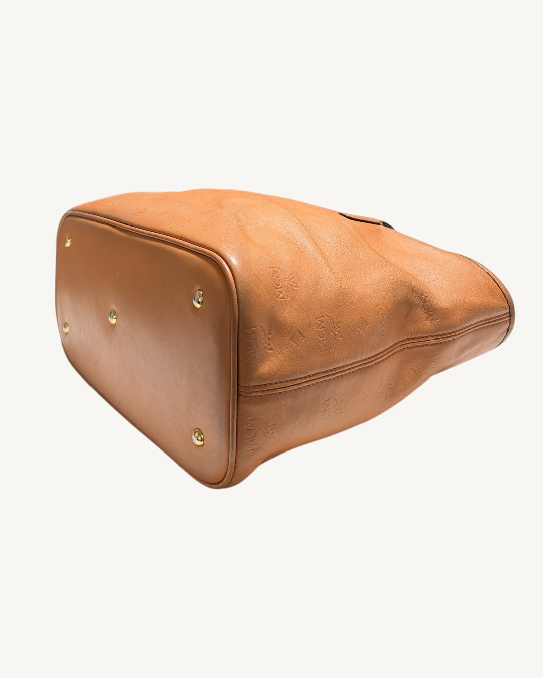 MCM tote base and side detail showing protective feet, rounded corner piping and embossed leather folds.