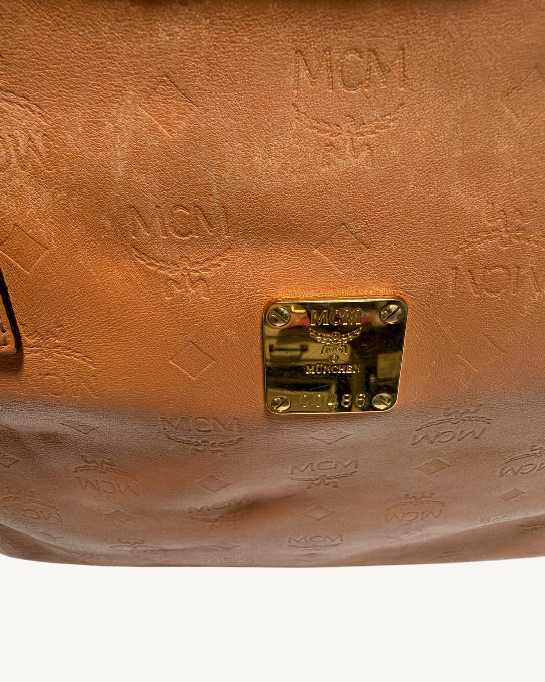 Close-up of MCM front plaque and surrounding embossed leather showing creases and variations in surface finish.