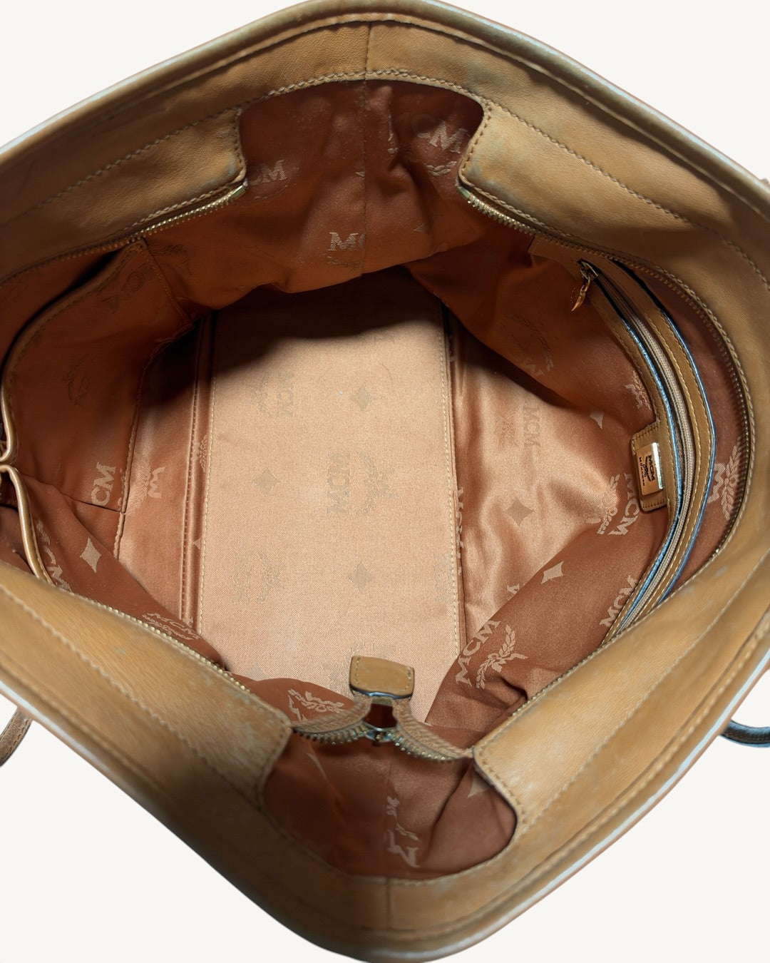 Overhead view inside MCM tote showing monogram lining, interior base marks, zip pocket and two open compartments.